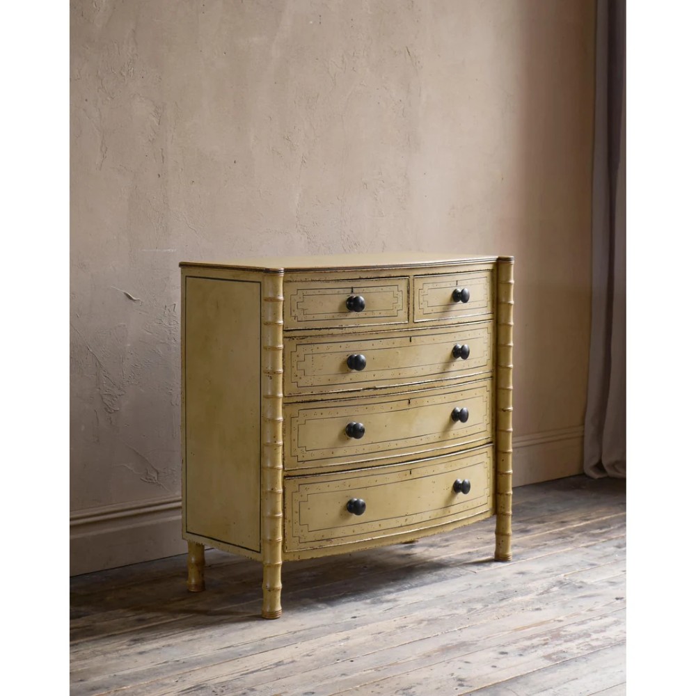 A Regency pale yellow painted chest of drawers featuring simulated bamboo turned corner columns and dark turned knobs.
