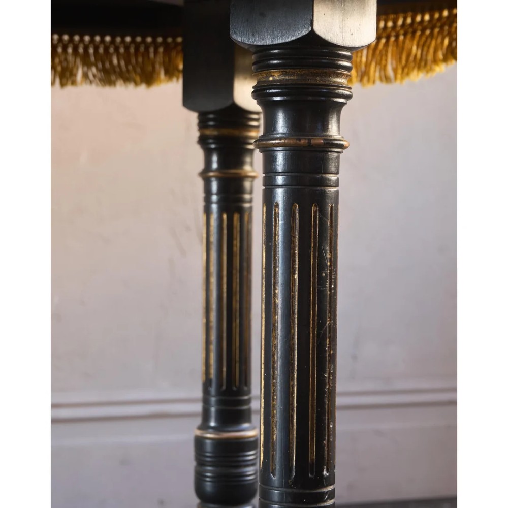 An octagonal Victorian centre table with ebonised turned legs, brass castors, and a pale top trimmed with fringe. View XIII