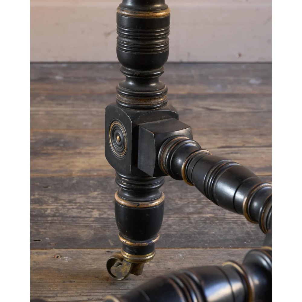 An octagonal Victorian centre table with ebonised turned legs, brass castors, and a pale top trimmed with fringe. View XIV