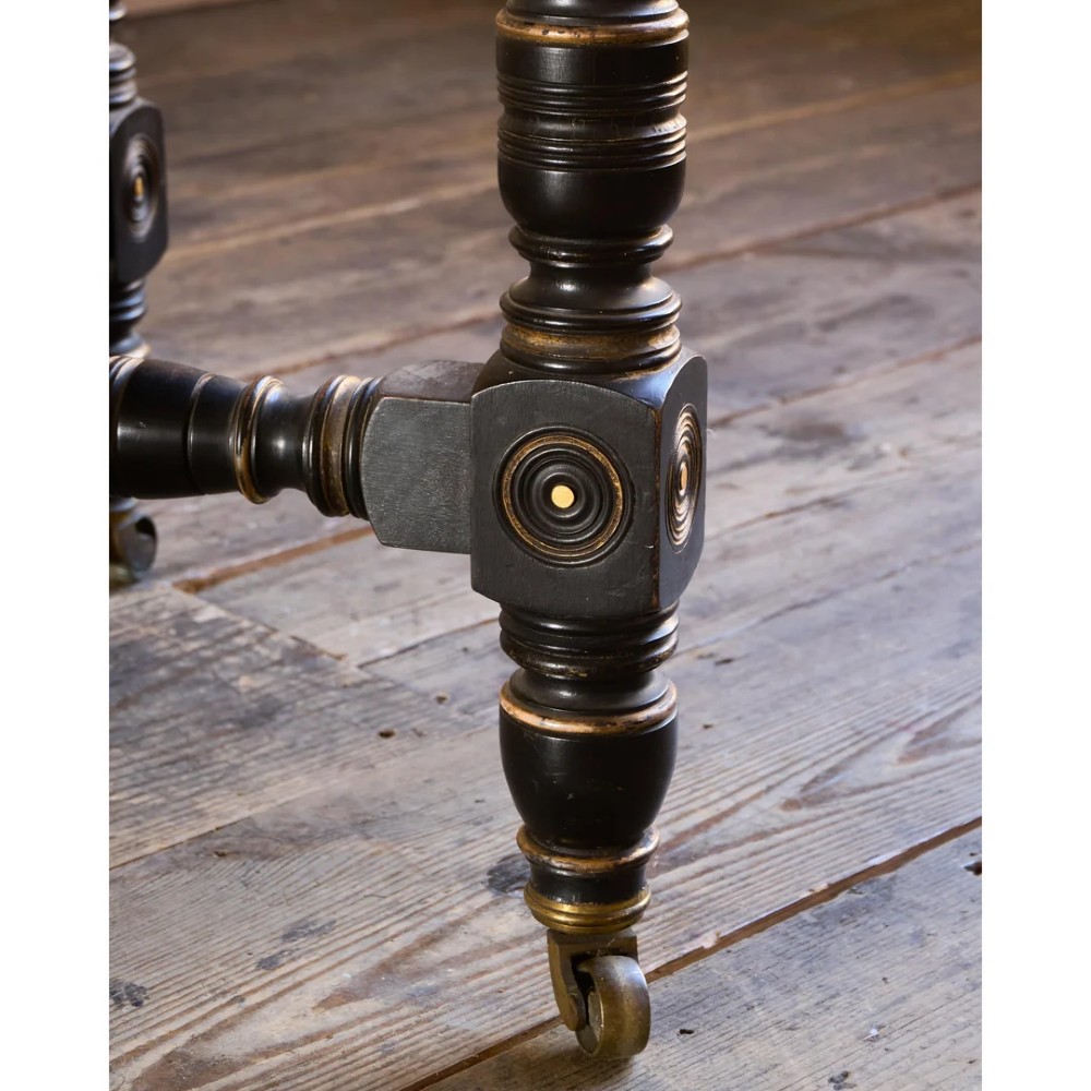 An octagonal Victorian centre table with ebonised turned legs, brass castors, and a pale top trimmed with fringe. View XV