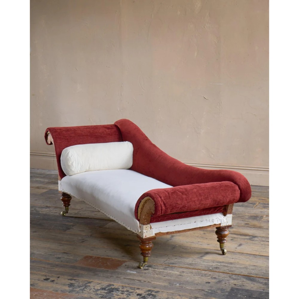 A Victorian asymmetrical chaise longue featuring red velvet and white calico fabric upholstery set on turned mahogany legs with brass castors.