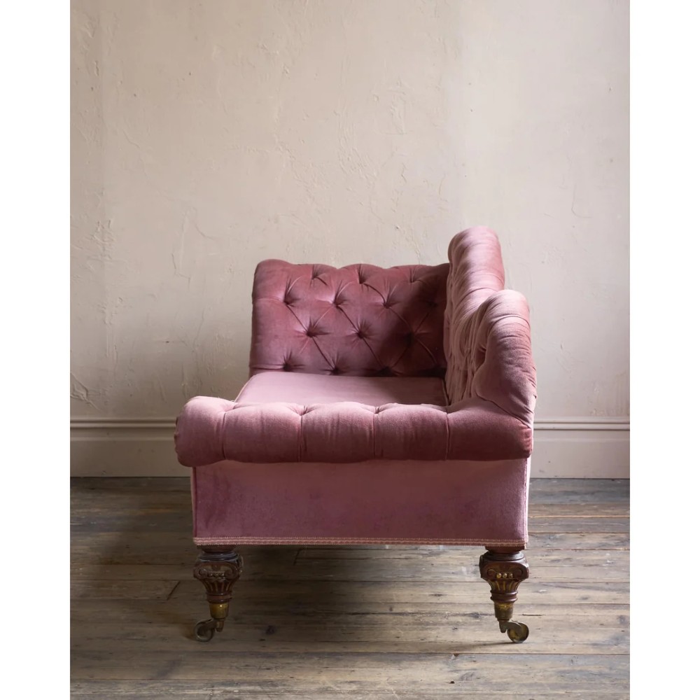 A Victorian deep-buttoned rose pink velvet chaise longue featuring carved mahogany Ionic column legs on brass castors with a loose white seat cushion. View IV