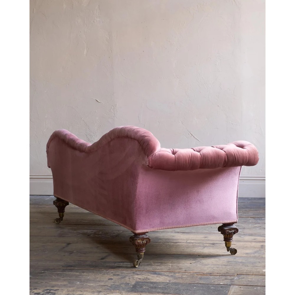 A Victorian deep-buttoned rose pink velvet chaise longue featuring carved mahogany Ionic column legs on brass castors with a loose white seat cushion. View VI