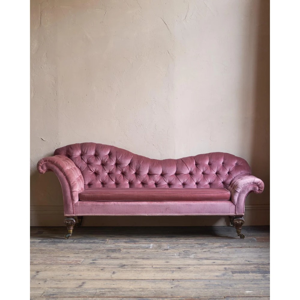 A Victorian deep-buttoned rose pink velvet chaise longue featuring carved mahogany Ionic column legs on brass castors with a loose white seat cushion. View VII