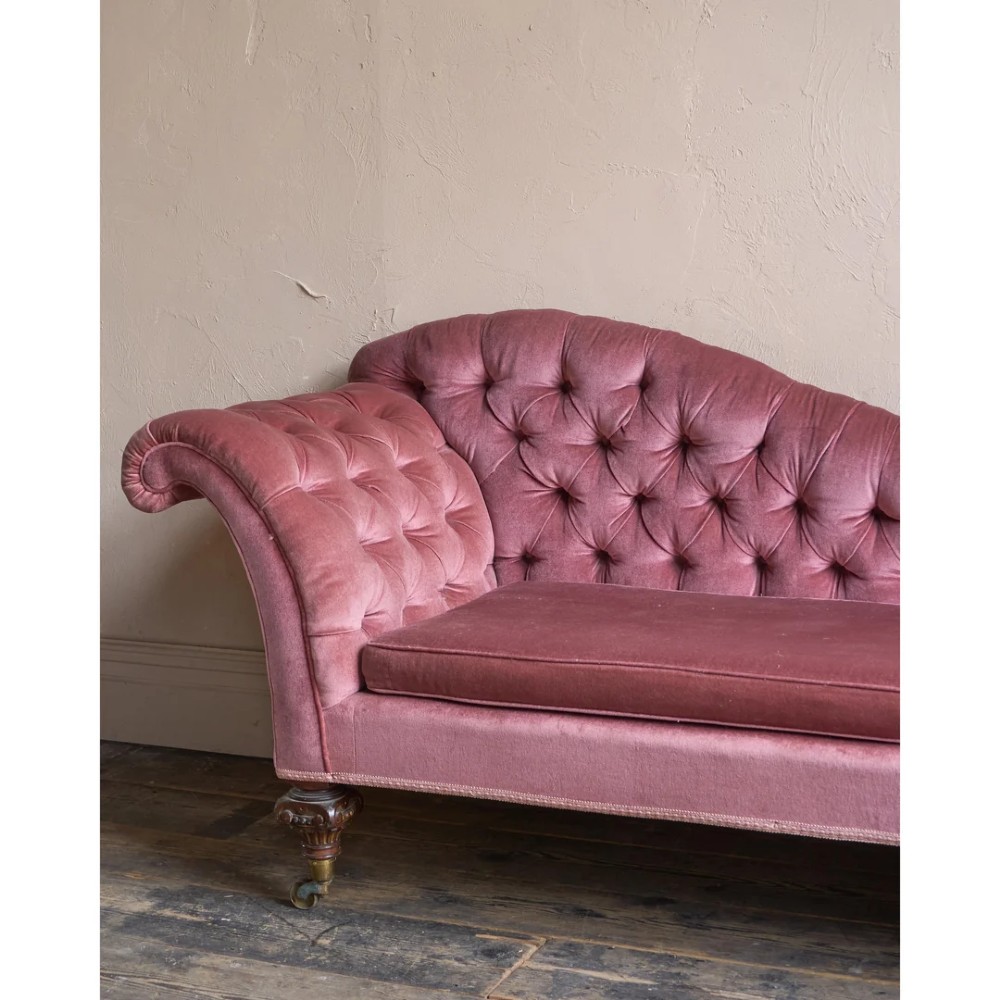 A Victorian deep-buttoned rose pink velvet chaise longue featuring carved mahogany Ionic column legs on brass castors with a loose white seat cushion. View VIII