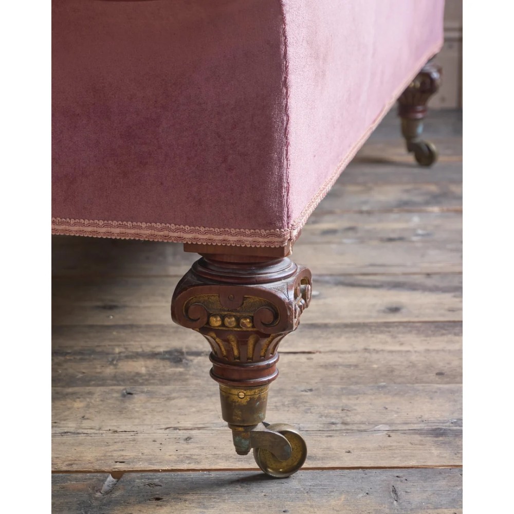 A Victorian deep-buttoned rose pink velvet chaise longue featuring carved mahogany Ionic column legs on brass castors with a loose white seat cushion. View X
