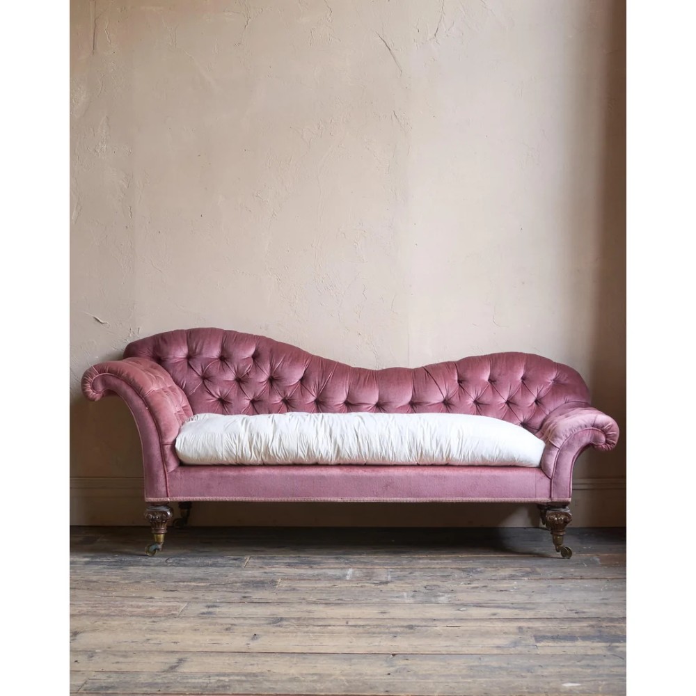 A Victorian deep-buttoned rose pink velvet chaise longue featuring carved mahogany Ionic column legs on brass castors with a loose white seat cushion. View XI