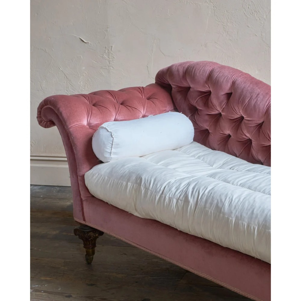 A Victorian deep-buttoned rose pink velvet chaise longue featuring carved mahogany Ionic column legs on brass castors with a loose white seat cushion. View XII