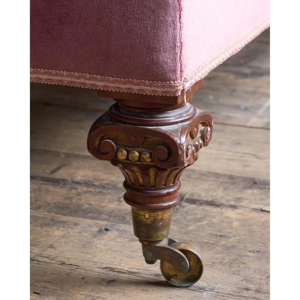 A Victorian deep-buttoned rose pink velvet chaise longue featuring carved mahogany Ionic column legs on brass castors with a loose white seat cushion. View XIII