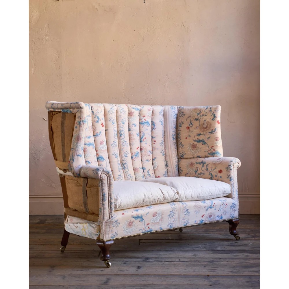 A nineteenth-century fluted wingback sofa featuring patterned floral upholstery, vertical channel tufting, and turned timber legs with brass castors.