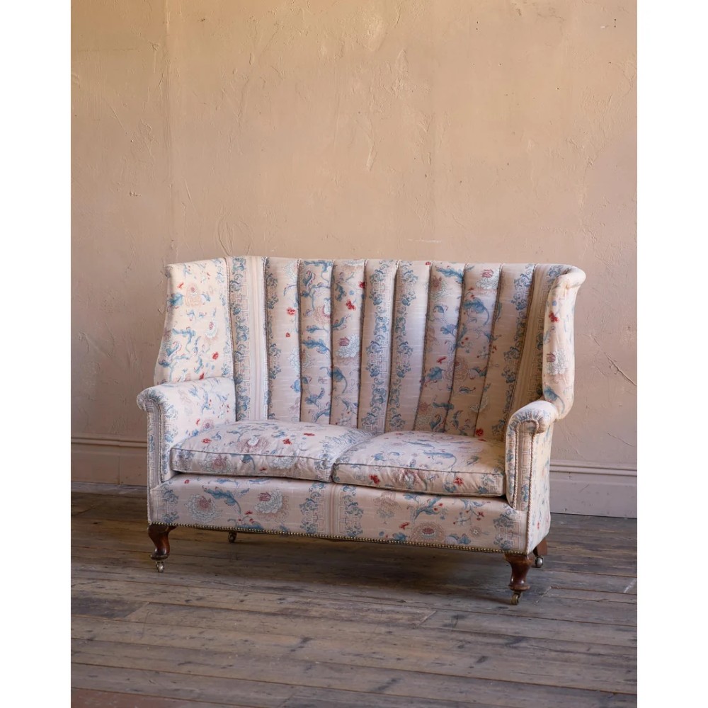 A nineteenth-century fluted wingback sofa featuring patterned floral upholstery, vertical channel tufting, and turned timber legs with brass castors. View II