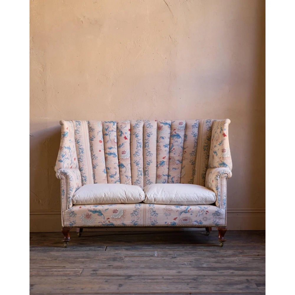 A nineteenth-century fluted wingback sofa featuring patterned floral upholstery, vertical channel tufting, and turned timber legs with brass castors. View III
