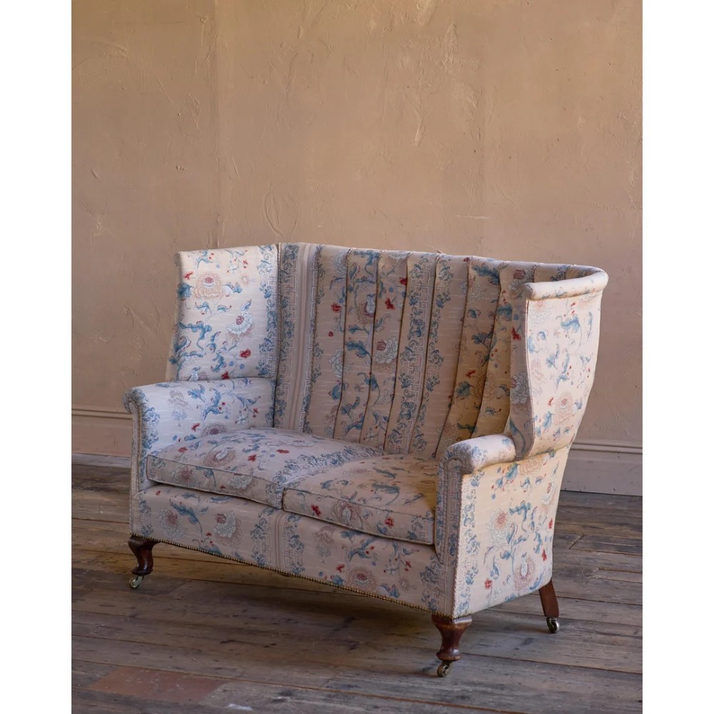 A nineteenth-century fluted wingback sofa featuring patterned floral upholstery, vertical channel tufting, and turned timber legs with brass castors. View IV