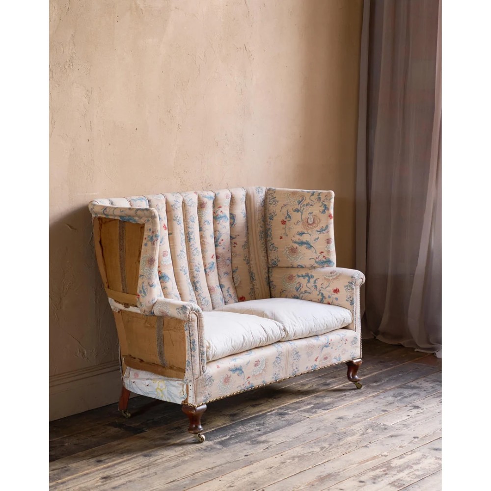 A nineteenth-century fluted wingback sofa featuring patterned floral upholstery, vertical channel tufting, and turned timber legs with brass castors. View XV