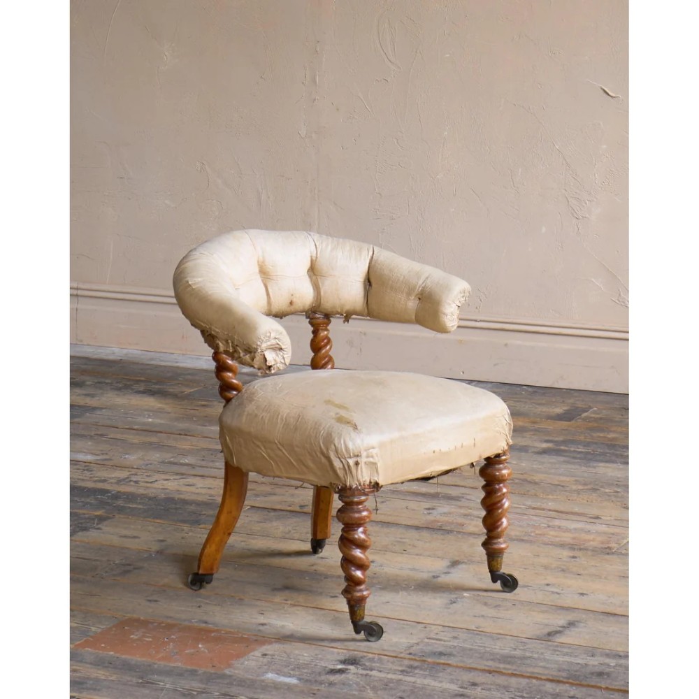 A Victorian low reading armchair with cream calico buttoned upholstery, spiral turned front legs, sabre rear legs, and brass castors.