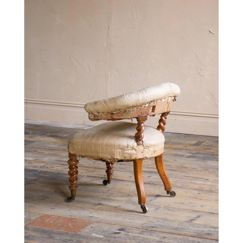 A Victorian low reading armchair with cream calico buttoned upholstery, spiral turned front legs, sabre rear legs, and brass castors. View III