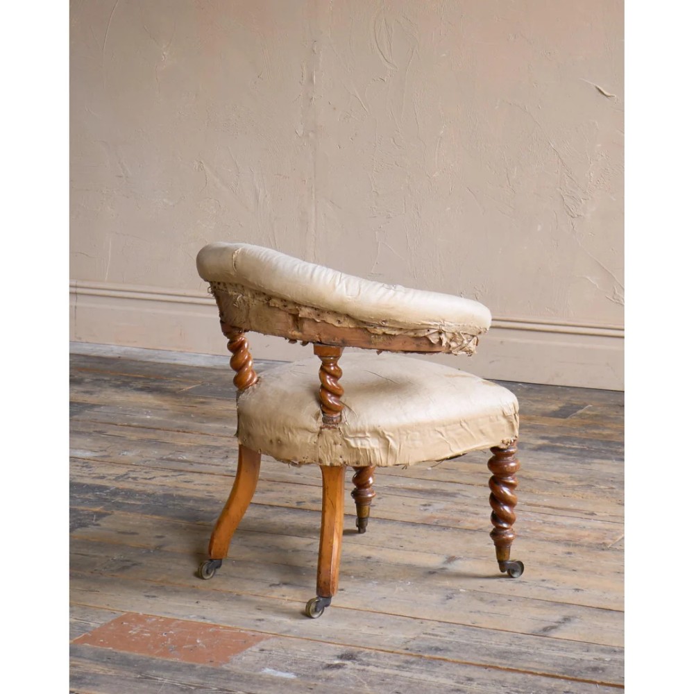 A Victorian low reading armchair with cream calico buttoned upholstery, spiral turned front legs, sabre rear legs, and brass castors. View IV
