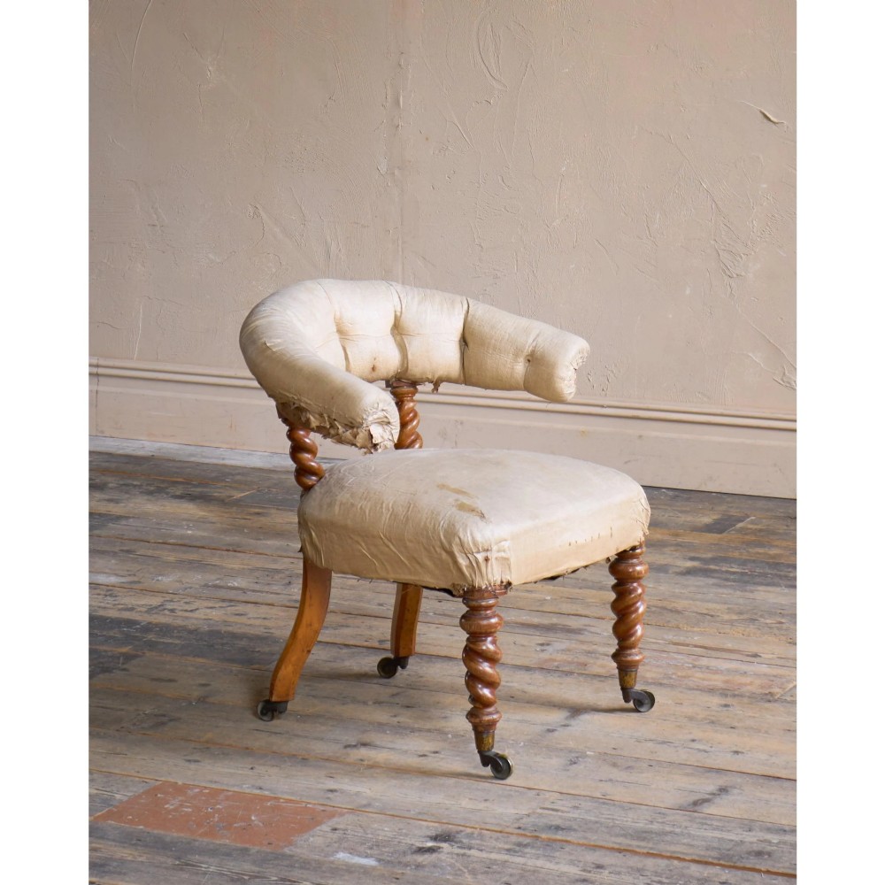 A Victorian low reading armchair with cream calico buttoned upholstery, spiral turned front legs, sabre rear legs, and brass castors. View V