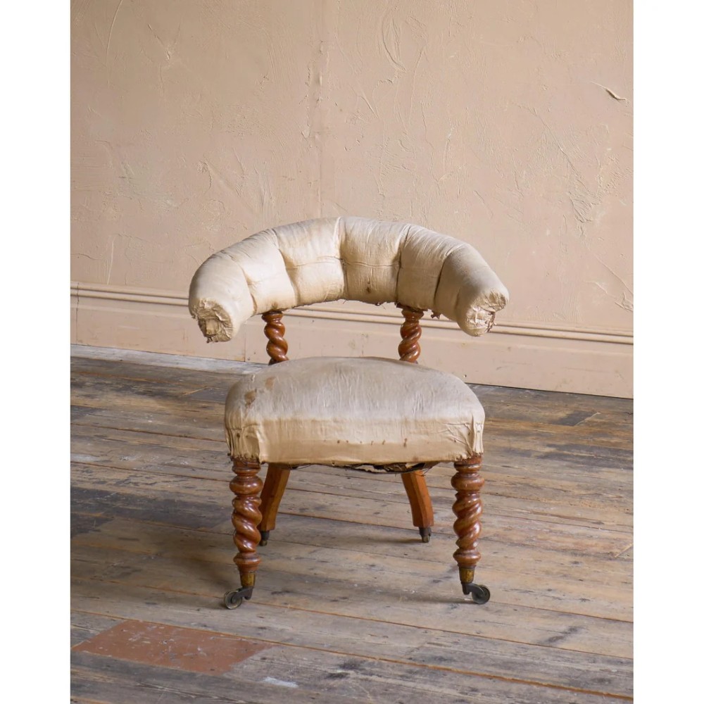 A Victorian low reading armchair with cream calico buttoned upholstery, spiral turned front legs, sabre rear legs, and brass castors. View VI