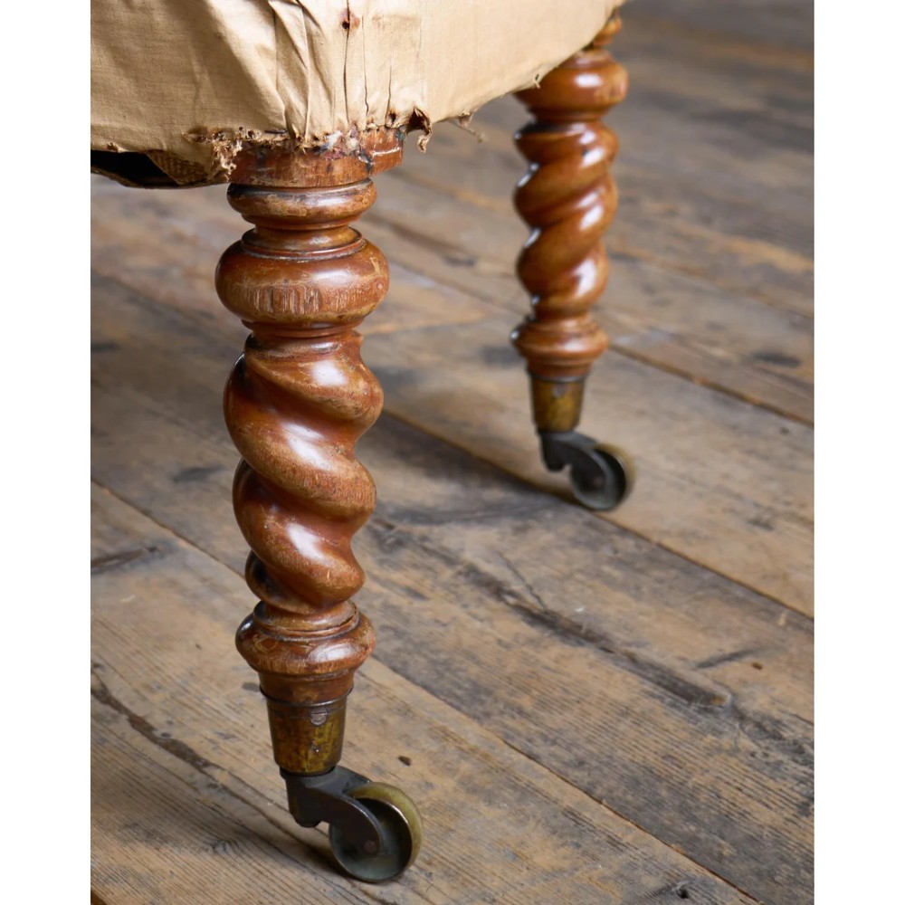 A Victorian low reading armchair with cream calico buttoned upholstery, spiral turned front legs, sabre rear legs, and brass castors. View VII