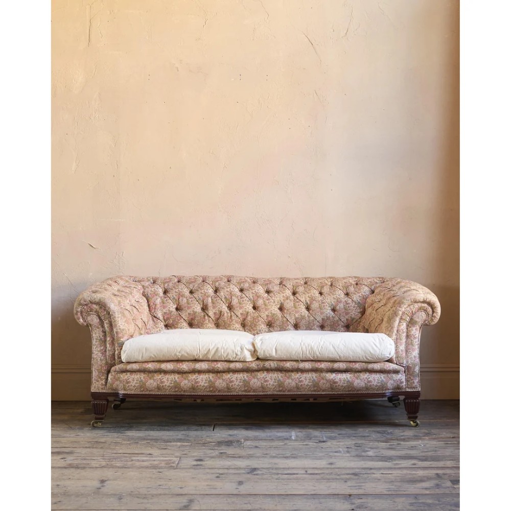A nineteenth-century Chesterfield sofa with patterned floral upholstery, deep button tufting on the backrest and rolled arms, loose seat cushions, and turned legs on brass castors.