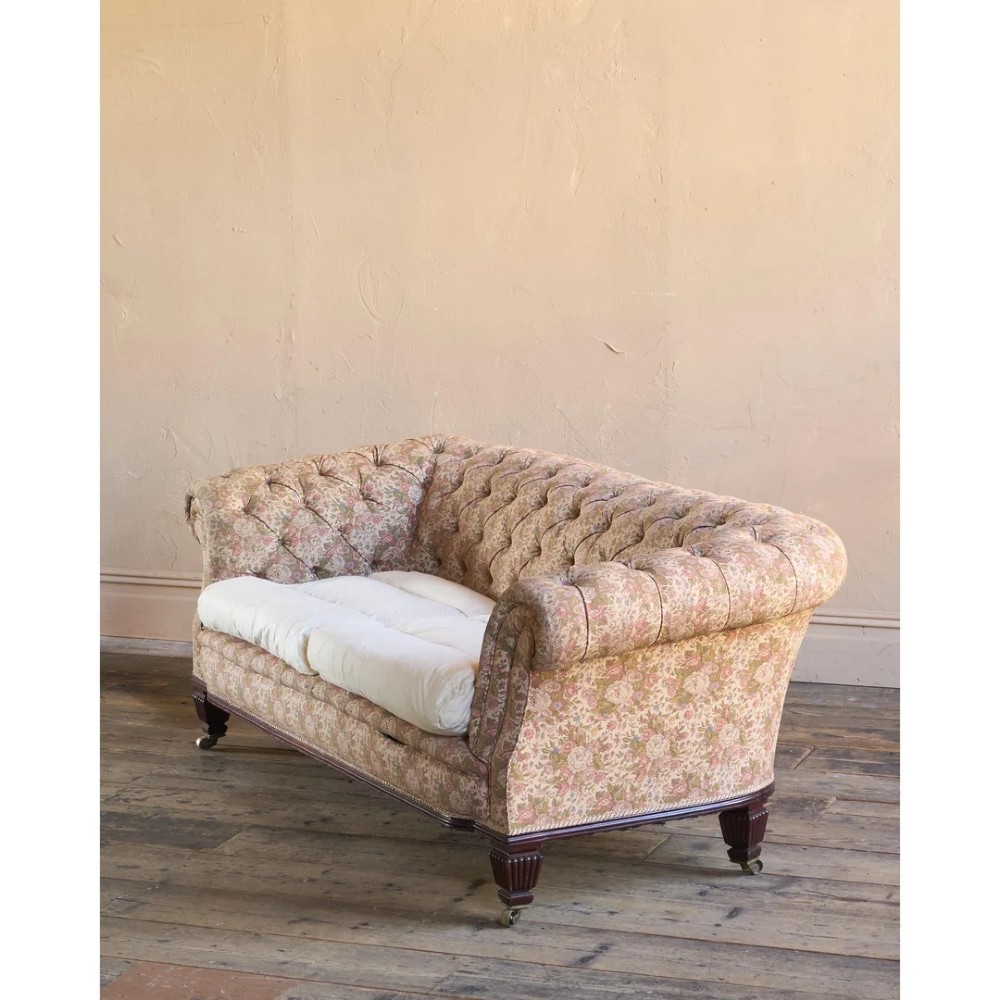 A nineteenth-century Chesterfield sofa with patterned floral upholstery, deep button tufting on the backrest and rolled arms, loose seat cushions, and turned legs on brass castors. View II