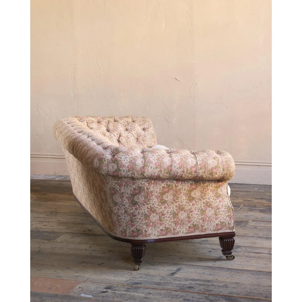 A nineteenth-century Chesterfield sofa with patterned floral upholstery, deep button tufting on the backrest and rolled arms, loose seat cushions, and turned legs on brass castors. View III