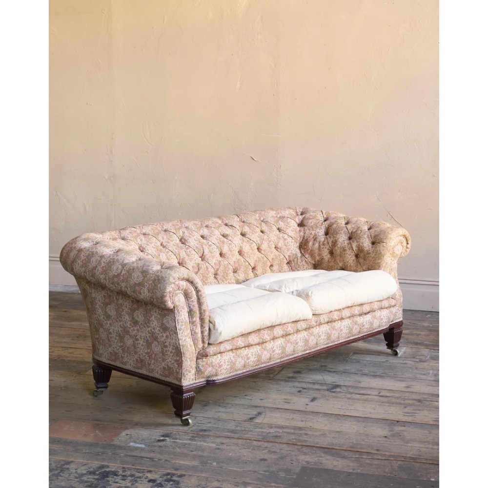 A nineteenth-century Chesterfield sofa with patterned floral upholstery, deep button tufting on the backrest and rolled arms, loose seat cushions, and turned legs on brass castors. View IV