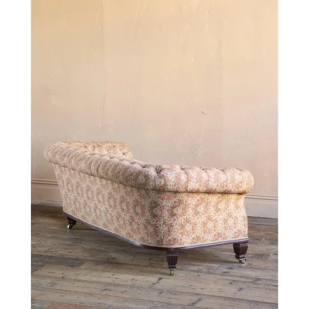 A nineteenth-century Chesterfield sofa with patterned floral upholstery, deep button tufting on the backrest and rolled arms, loose seat cushions, and turned legs on brass castors. View VI