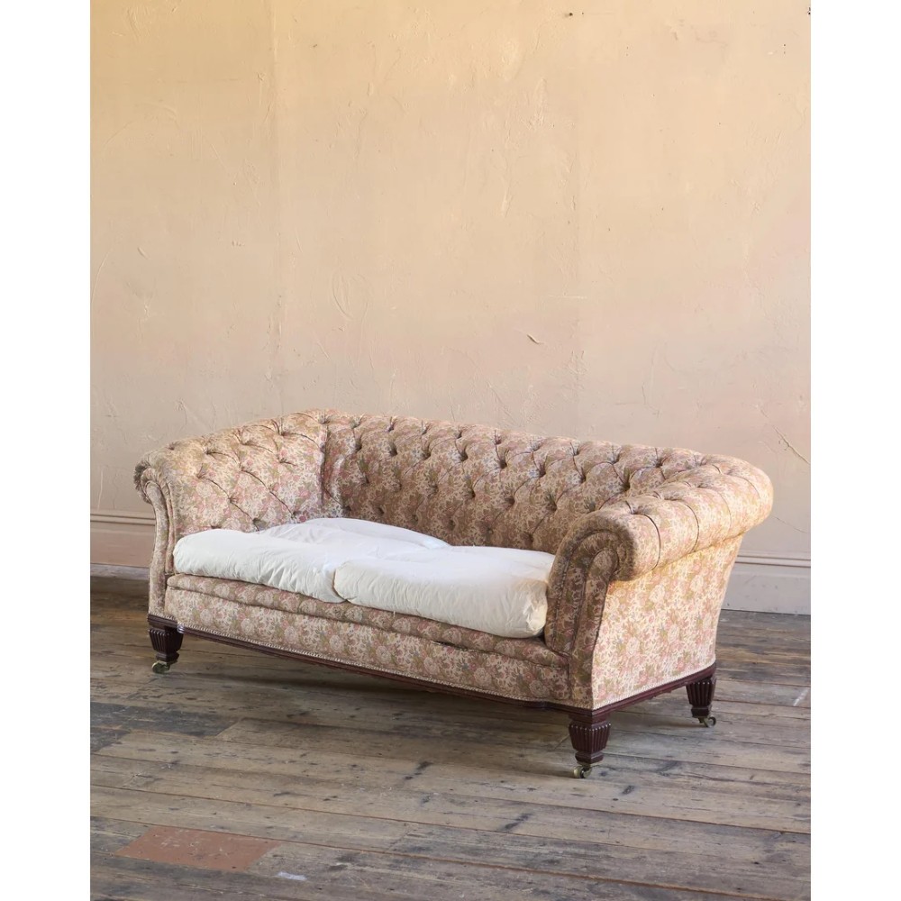 A nineteenth-century Chesterfield sofa with patterned floral upholstery, deep button tufting on the backrest and rolled arms, loose seat cushions, and turned legs on brass castors. View VII