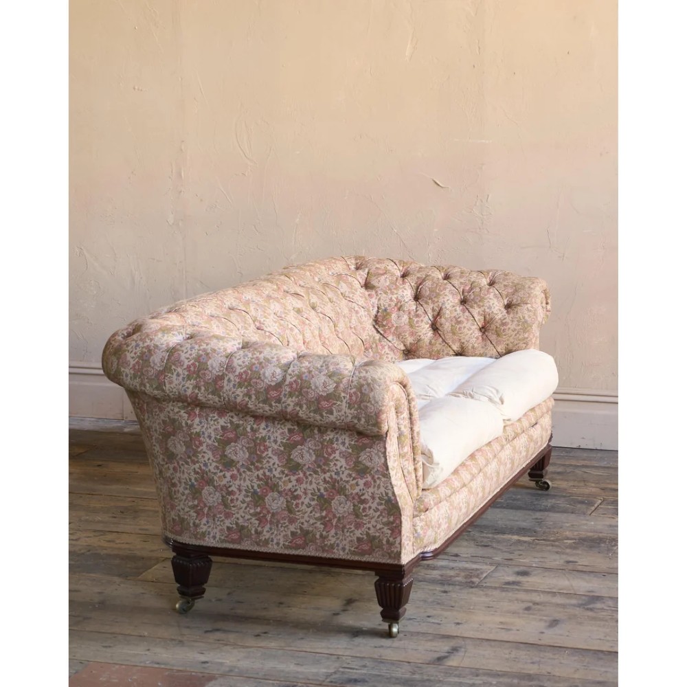 A nineteenth-century Chesterfield sofa with patterned floral upholstery, deep button tufting on the backrest and rolled arms, loose seat cushions, and turned legs on brass castors. View VIII