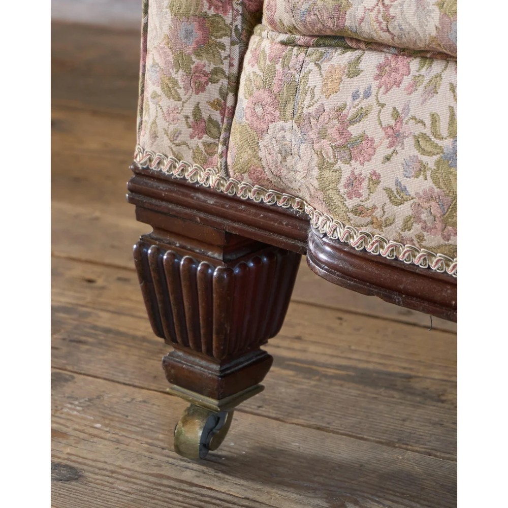 A nineteenth-century Chesterfield sofa with patterned floral upholstery, deep button tufting on the backrest and rolled arms, loose seat cushions, and turned legs on brass castors. View X