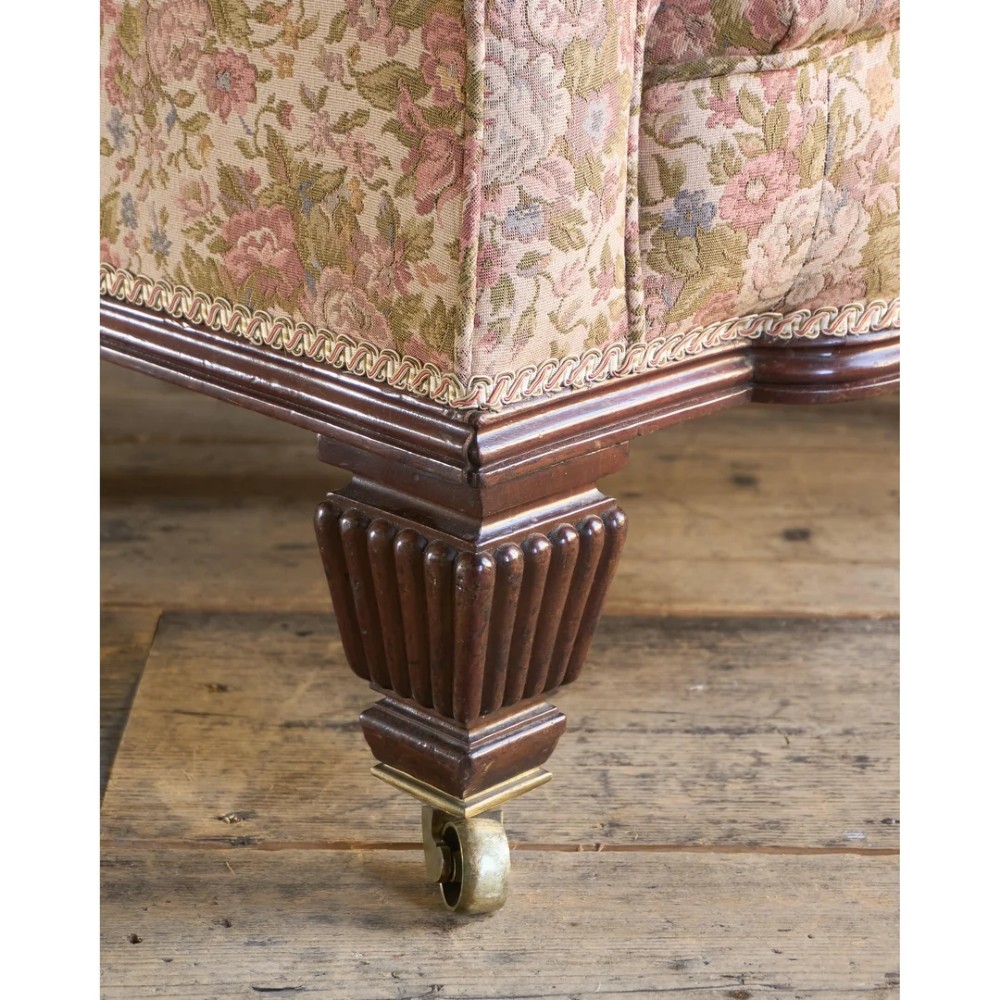 A nineteenth-century Chesterfield sofa with patterned floral upholstery, deep button tufting on the backrest and rolled arms, loose seat cushions, and turned legs on brass castors. View XI