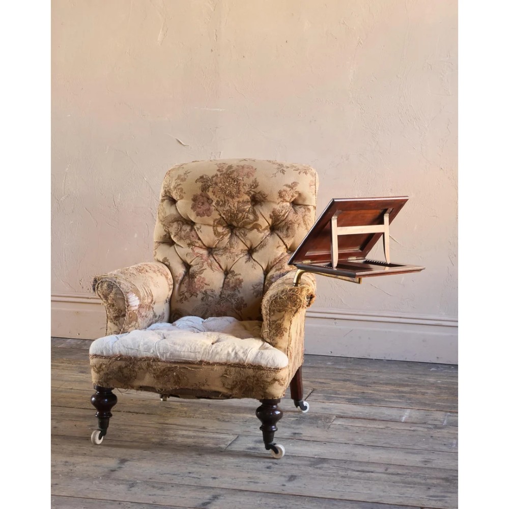 A 19th-century Victorian library armchair upholstered in beige floral pattern fabric with deep buttoning, turned front legs on castors, and an attached adjustable mahogany reading stand. View IV
