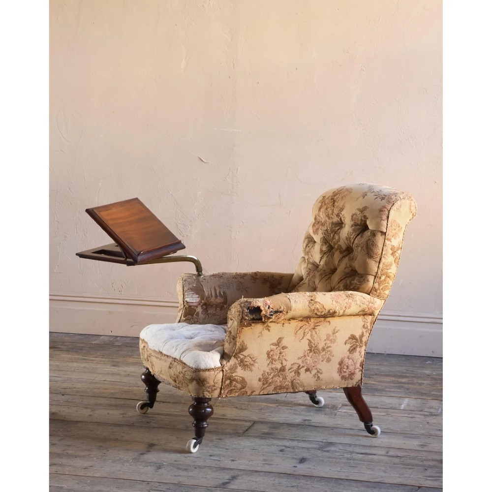 A 19th-century Victorian library armchair upholstered in beige floral pattern fabric with deep buttoning, turned front legs on castors, and an attached adjustable mahogany reading stand. View V