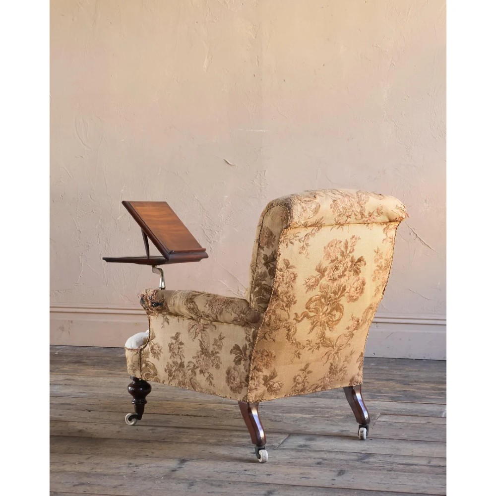 A 19th-century Victorian library armchair upholstered in beige floral pattern fabric with deep buttoning, turned front legs on castors, and an attached adjustable mahogany reading stand. View VI