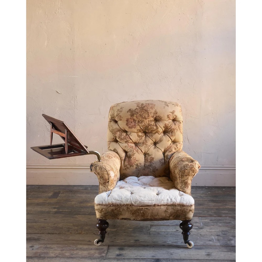 A 19th-century Victorian library armchair upholstered in beige floral pattern fabric with deep buttoning, turned front legs on castors, and an attached adjustable mahogany reading stand. View VIII