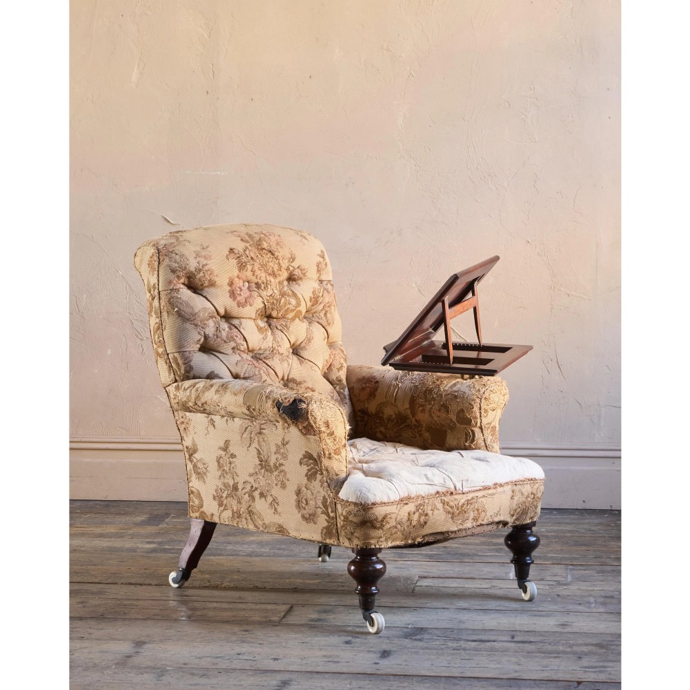 A 19th-century Victorian library armchair upholstered in beige floral pattern fabric with deep buttoning, turned front legs on castors, and an attached adjustable mahogany reading stand. View IX