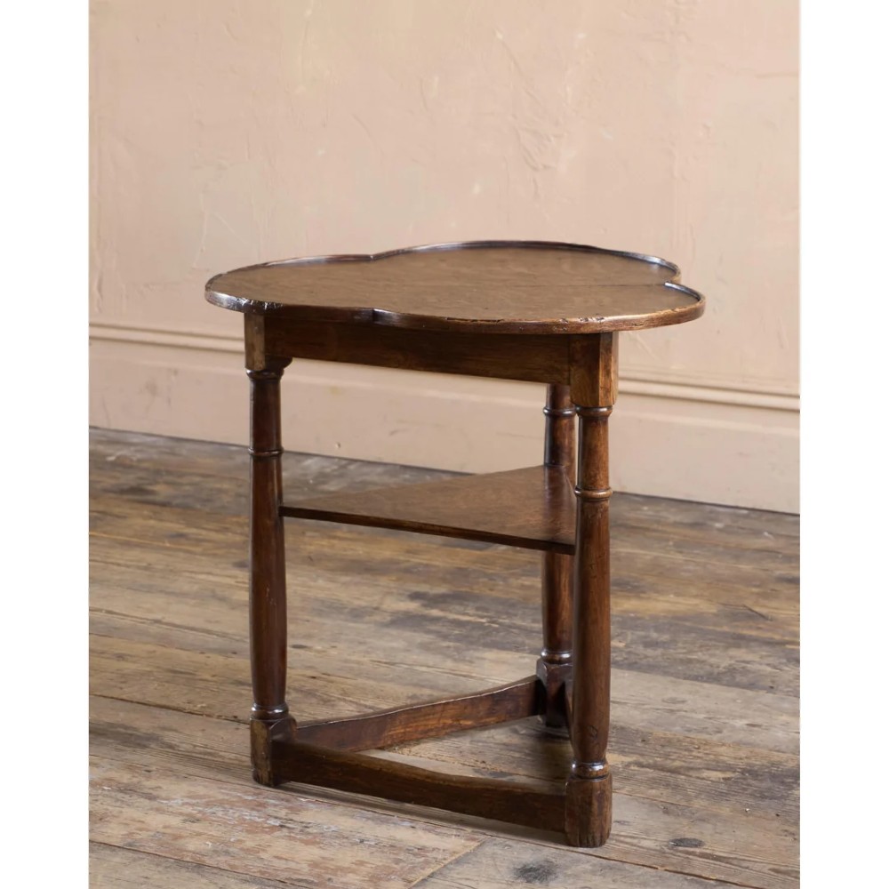 An 18th-century dark oak cricket table featuring a trefoil-shaped top, three turned legs, a triangular lower shelf, and a stretcher base. View V