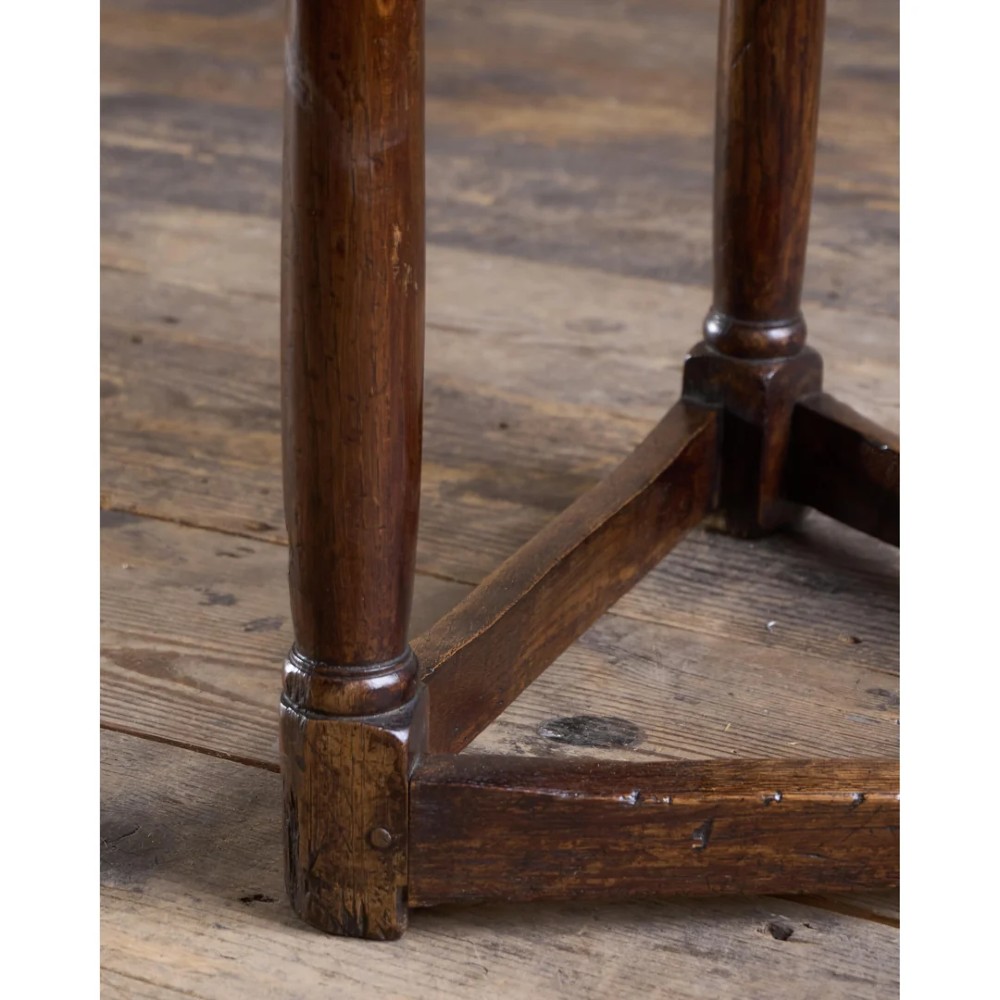 An 18th-century dark oak cricket table featuring a trefoil-shaped top, three turned legs, a triangular lower shelf, and a stretcher base. View VI