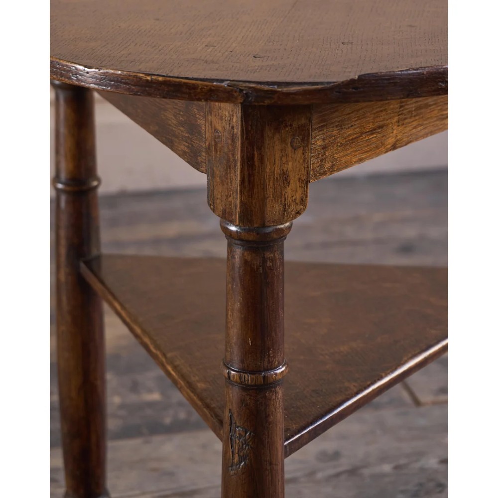 An 18th-century dark oak cricket table featuring a trefoil-shaped top, three turned legs, a triangular lower shelf, and a stretcher base. View X