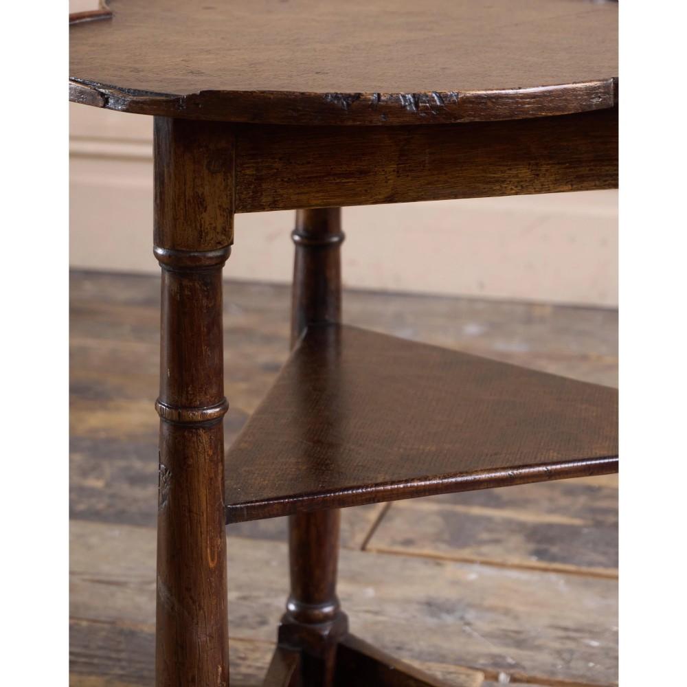 An 18th-century dark oak cricket table featuring a trefoil-shaped top, three turned legs, a triangular lower shelf, and a stretcher base. View XI