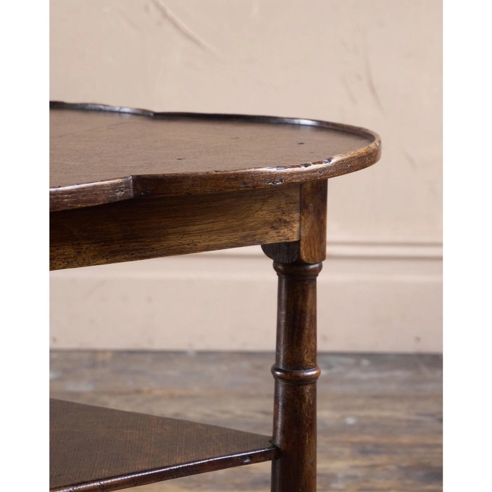An 18th-century dark oak cricket table featuring a trefoil-shaped top, three turned legs, a triangular lower shelf, and a stretcher base. View XII