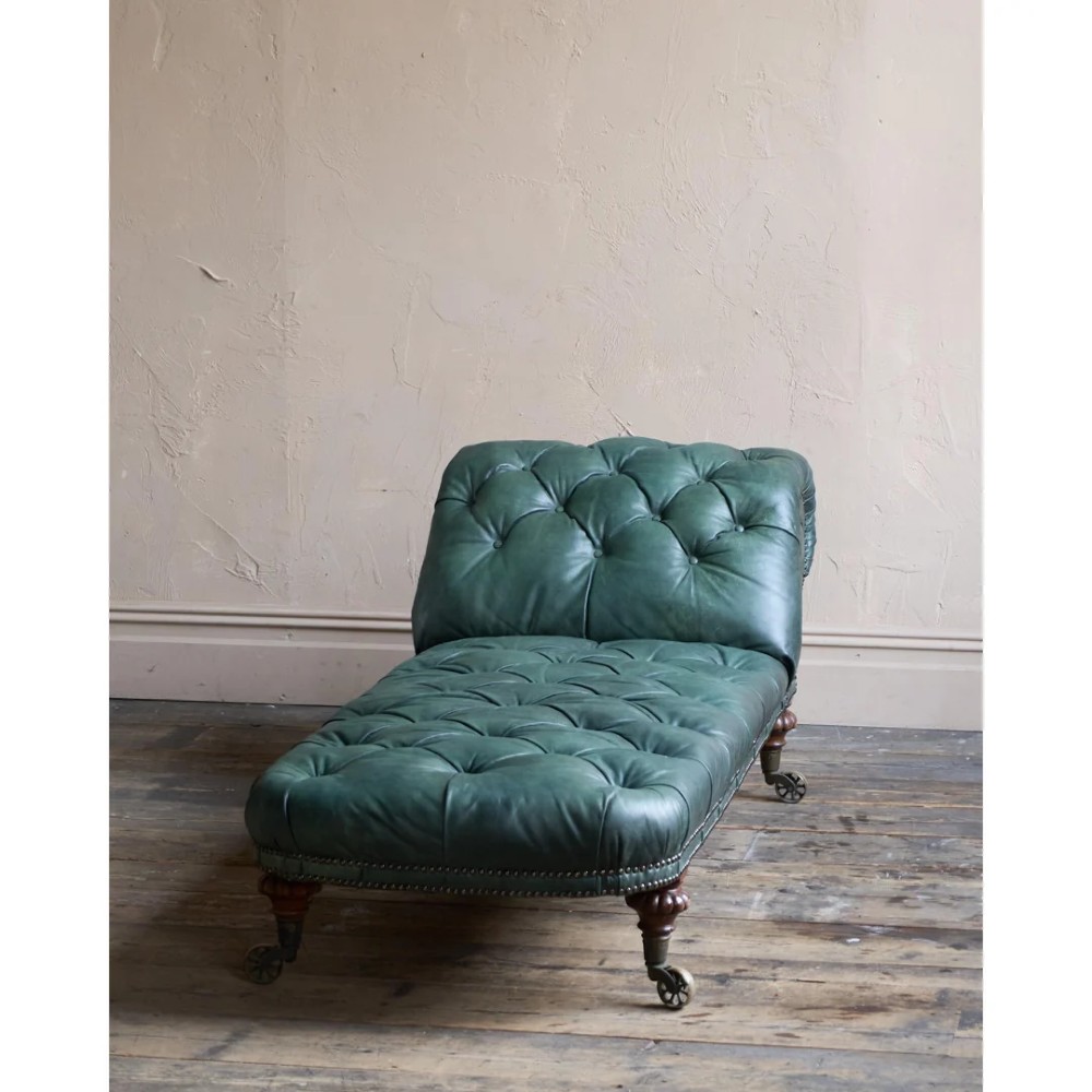A deep buttoned green leather chaise longue featuring brass stud details, turned wood legs, and brass castors. View II