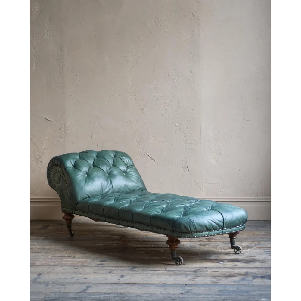 A deep buttoned green leather chaise longue featuring brass stud details, turned wood legs, and brass castors. View IV