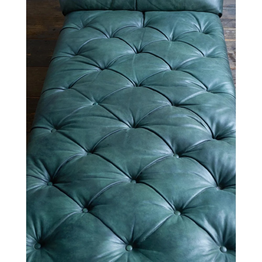 A deep buttoned green leather chaise longue featuring brass stud details, turned wood legs, and brass castors. View VIII