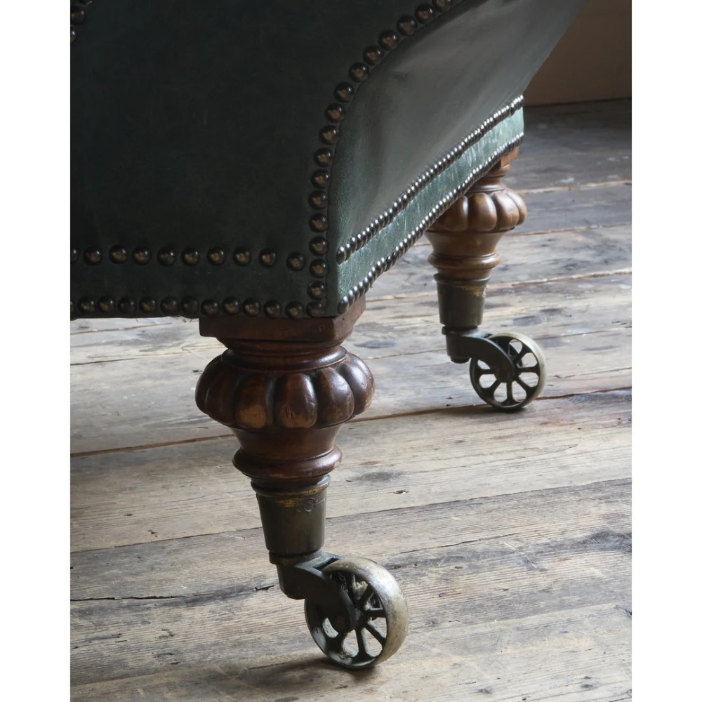 A deep buttoned green leather chaise longue featuring brass stud details, turned wood legs, and brass castors. View XI
