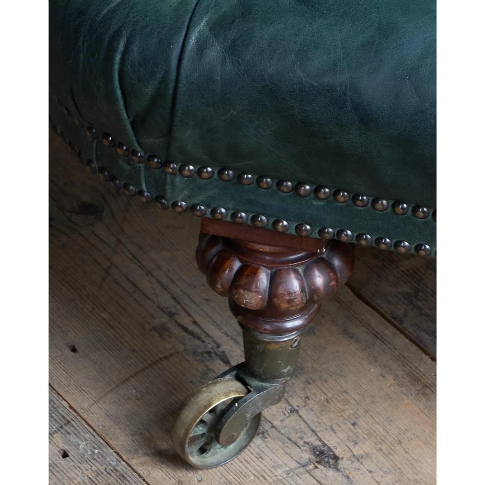 A deep buttoned green leather chaise longue featuring brass stud details, turned wood legs, and brass castors. View XII