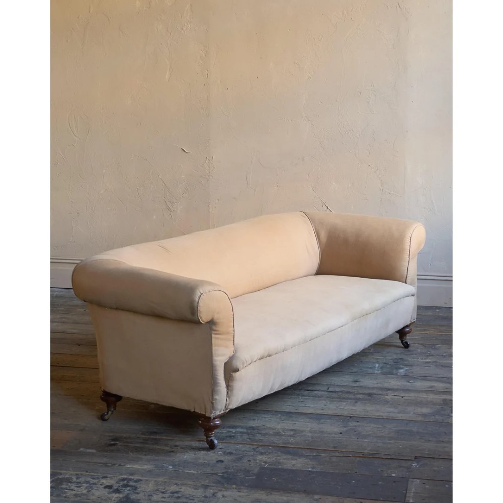 A 19th-century Chesterfield sofa upholstered in neutral beige calico fabric featuring rolled arms and turned wooden legs on brass castors.