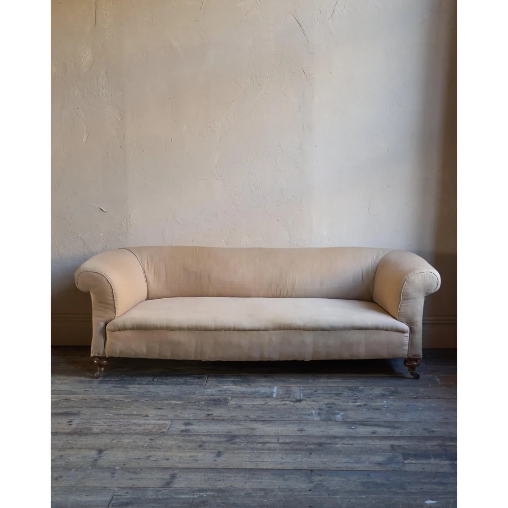 A 19th-century Chesterfield sofa upholstered in neutral beige calico fabric featuring rolled arms and turned wooden legs on brass castors. View II